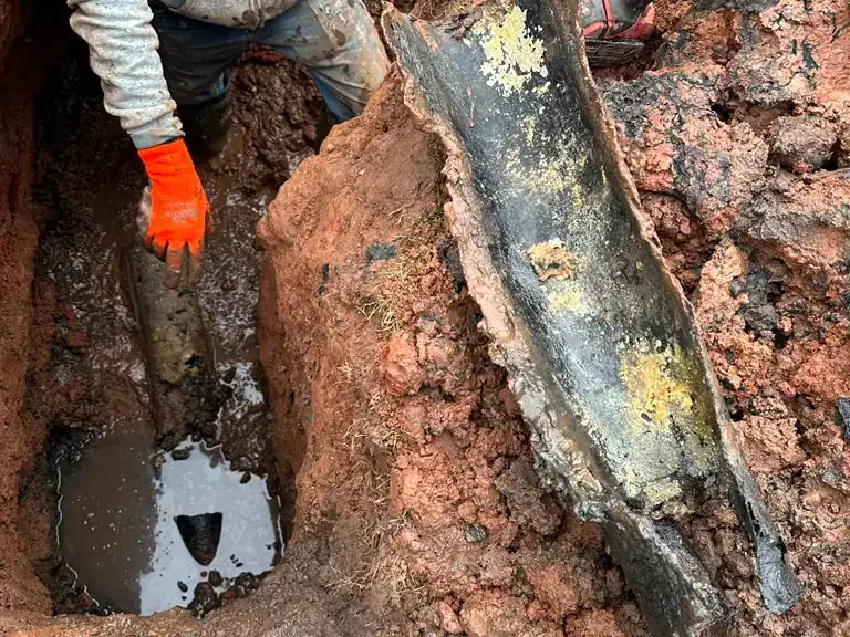 Technician removing a broken, corroded cast-iron sewer pipe section from an excavated trench — sewer line repair in Walpack, NJ