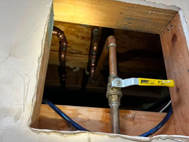 New copper pipe section and shut-off valve installed through a wall access opening — broken pipe repair in Central New Jersey