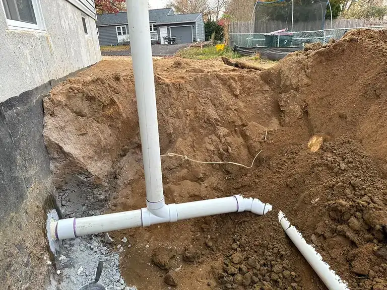 New PVC sewer piping assembled in an exterior excavation at the foundation of a house — sewer line repair in Plumsted, NJ
