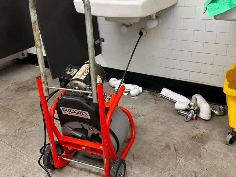Clogged kitchen sink drain cleared with a drum cable machine at the open cabinet — drain cleaning in Dennis Township, NJ