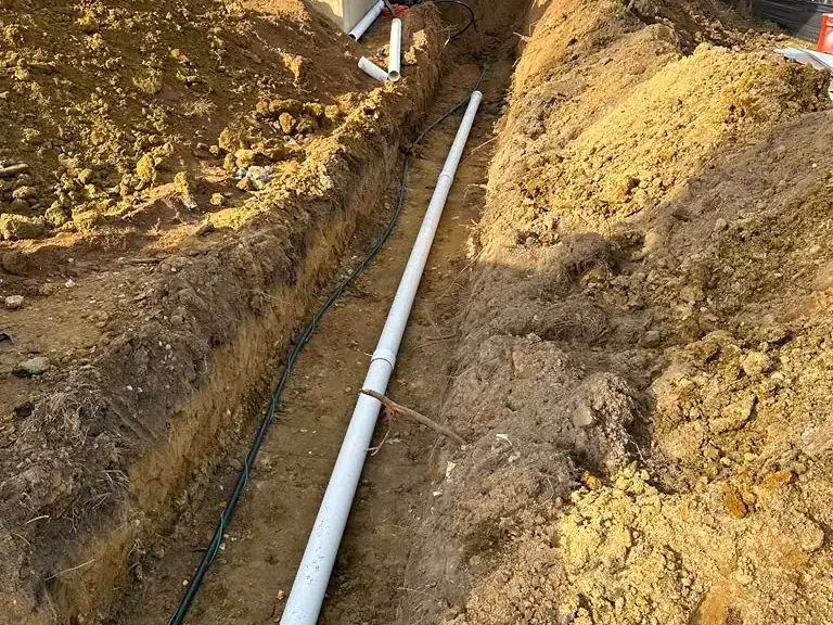 New PVC sewer line installed in an excavated trench along the foundation of a home — Sewer Line Repair & Replacement in Eatontown